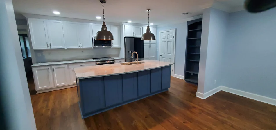 Kitchen remodel featuring a navy blue island, white cabinetry, pendant lighting, and dark hardwood flooring.