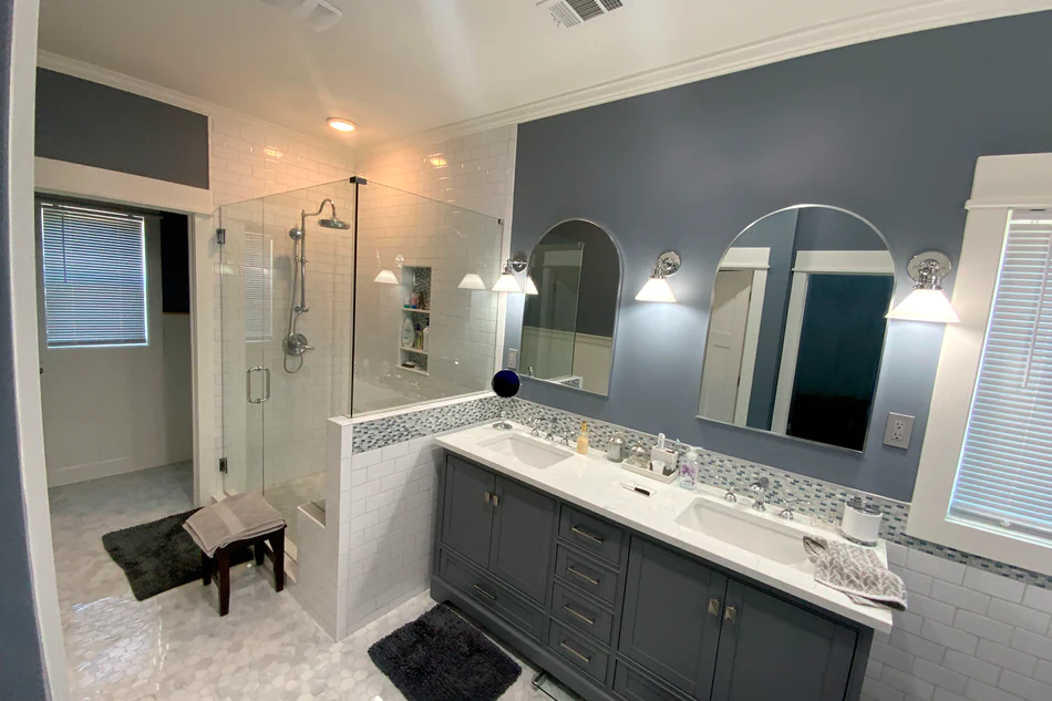 Bathroom remodel featuring navy walls, arched mirrors, a dark double vanity, and a glass-enclosed shower.