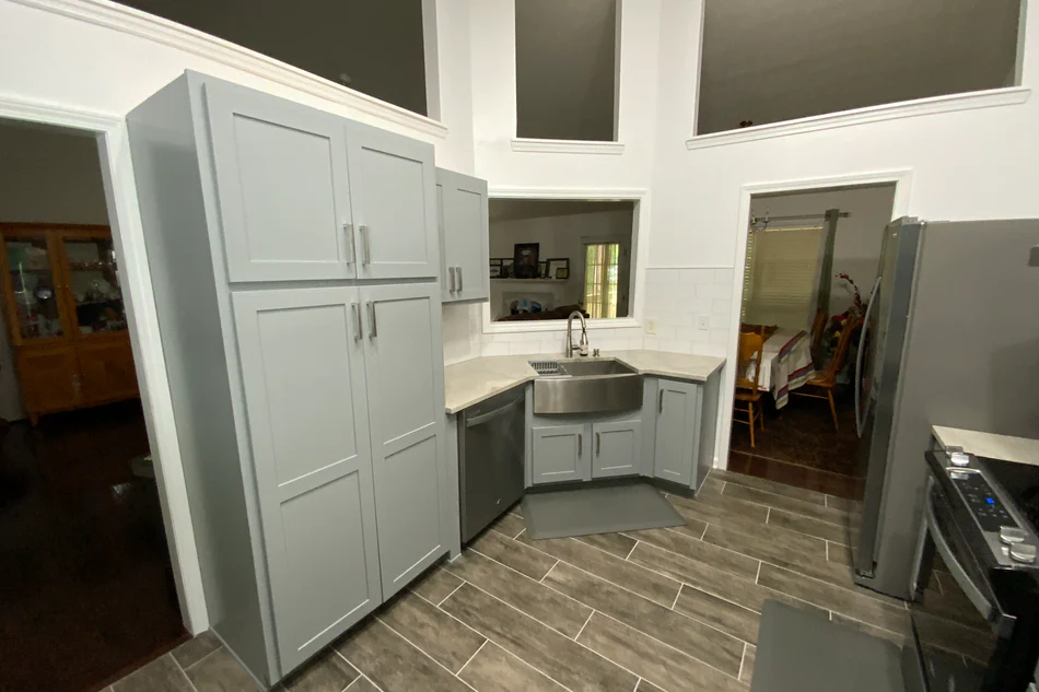 Gray galley kitchen featuring tall pantry cabinets, a corner sink, and wood-look tile flooring.