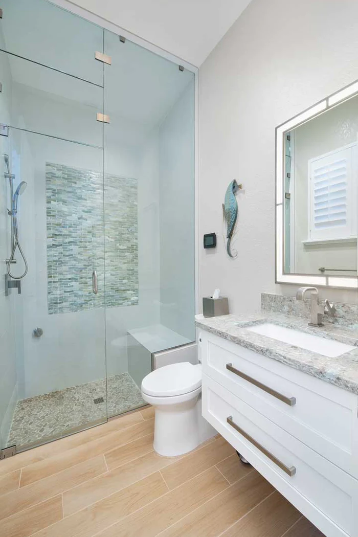 Modern bathroom remodel with a glass-enclosed shower, pebble flooring, stone tile accents, white vanity, and contemporary fixtures.