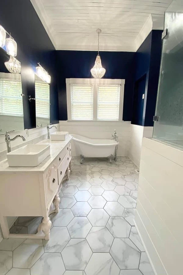 Elegant bathroom remodel featuring a white clawfoot tub, vintage-style double vanity, marble-look hexagonal flooring, and crystal pendant lighting.